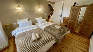 Un lit double avec deux oreillers et une couverture, un plancher en bois, une armoire en bois et une porte donnant sur un escalier.