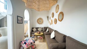 A living room with a brown sofa, a round coffee table, and a wicker chair. There are decorative wall mirrors and a wicker ceiling light. - Riad Abi - magical view and swimming pool - Free breakfast (Marrakech)