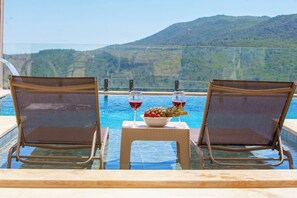 Two lounge chairs facing a pool with a table between them, holding a bowl of fruit and two glasses of red wine. - Huzurun adresi (antalya kas)