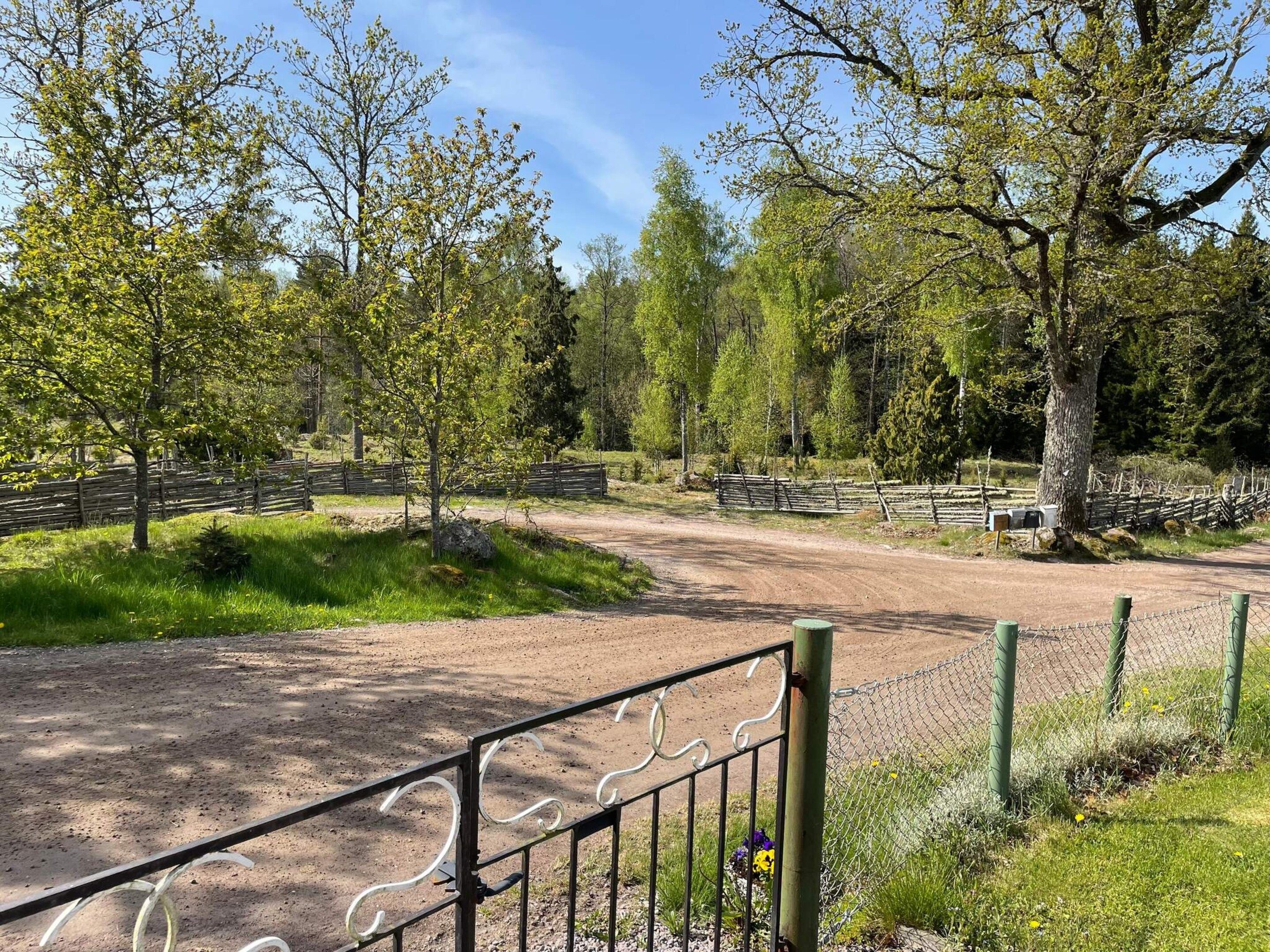 Un sendero de tierra que atraviesa un área cercada con árboles y cielo despejado.