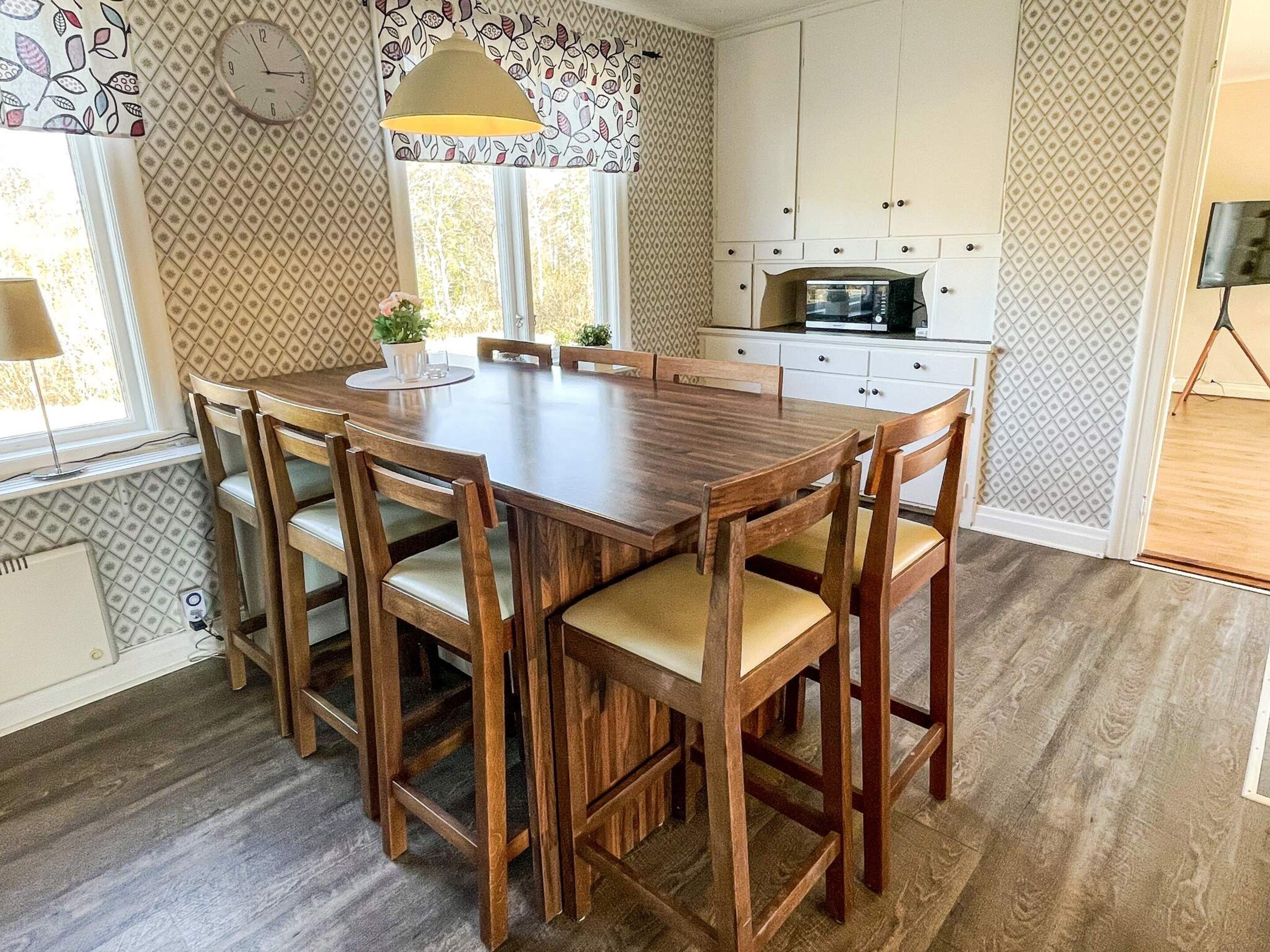 A dining area with a wooden table and chairs, a clock on the wall, and a window with curtains.