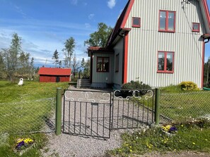 Une maison à deux étages avec un toit rouge, une allée en gravier et un portail en métal.