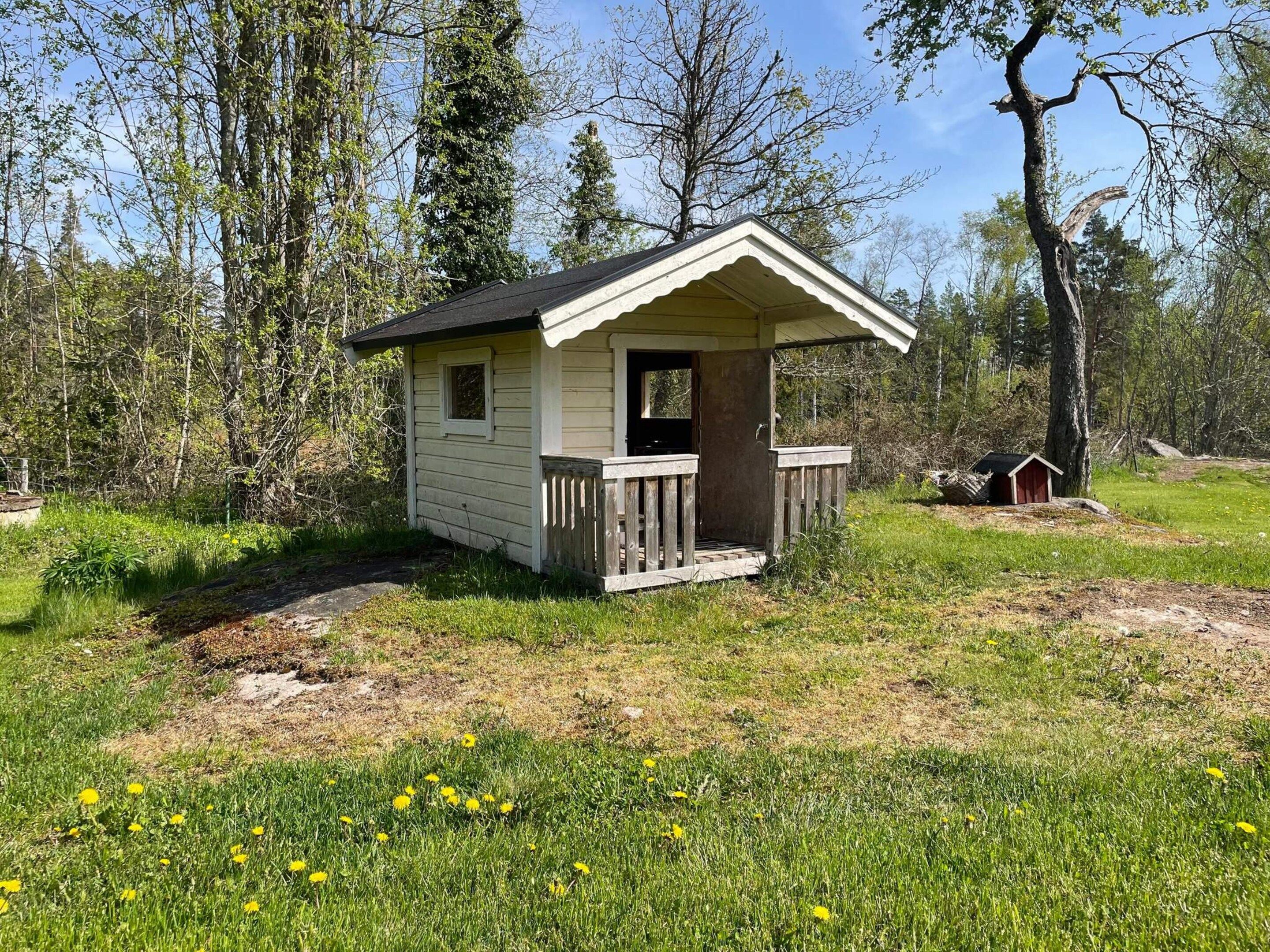 A small wooden cabin with a porch, surrounded by trees and grass.