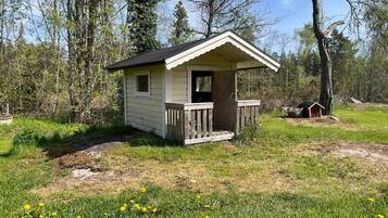 A small wooden cabin with a porch, surrounded by trees and grass.