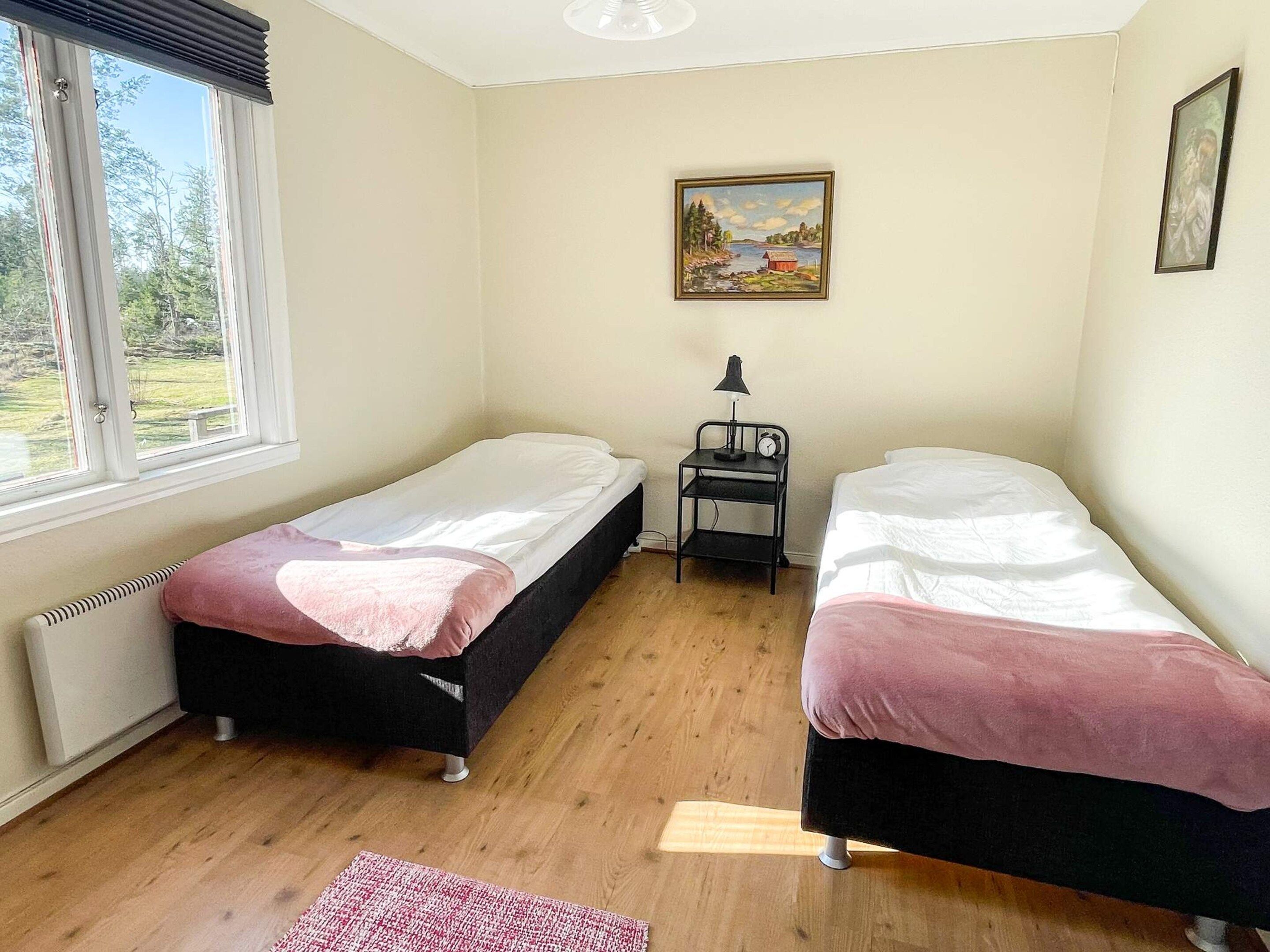 Una habitación con dos camas individuales, una mesita con una lámpara, un cuadro en la pared y una ventana con vistas a la vegetación.