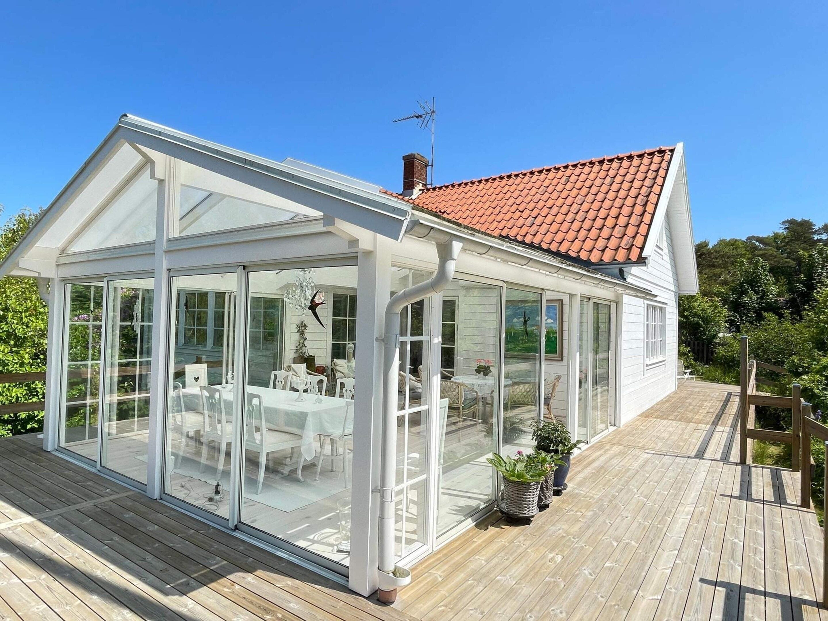 Ein Wintergarten mit geflastertem Dach, Glaswänden und einer Holzdielen-Terrasse.