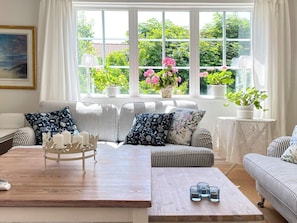 A living room with a sofa set, a coffee table, and a view of greenery through large windows. - 5 Star Holiday Home in Mellbystrand (Mellbystrand)