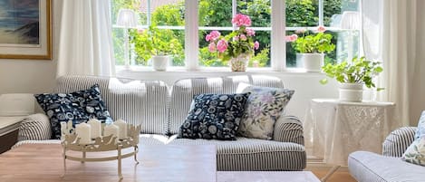 A cozy living room with striped sofas, a wooden coffee table, and a view of a garden through large windows.