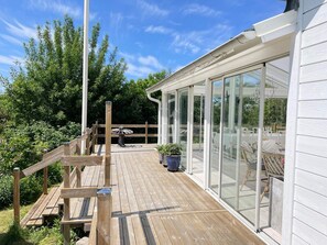 A wooden deck with a glass-enclosed patio area, a metal table, and potted plants. - 5 Star Holiday Home in Mellbystrand (Mellbystrand)