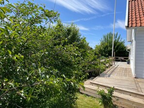 A wooden deck leading to a white building with a red roof, surrounded by lush greenery. - 5 Star Holiday Home in Mellbystrand (Mellbystrand)