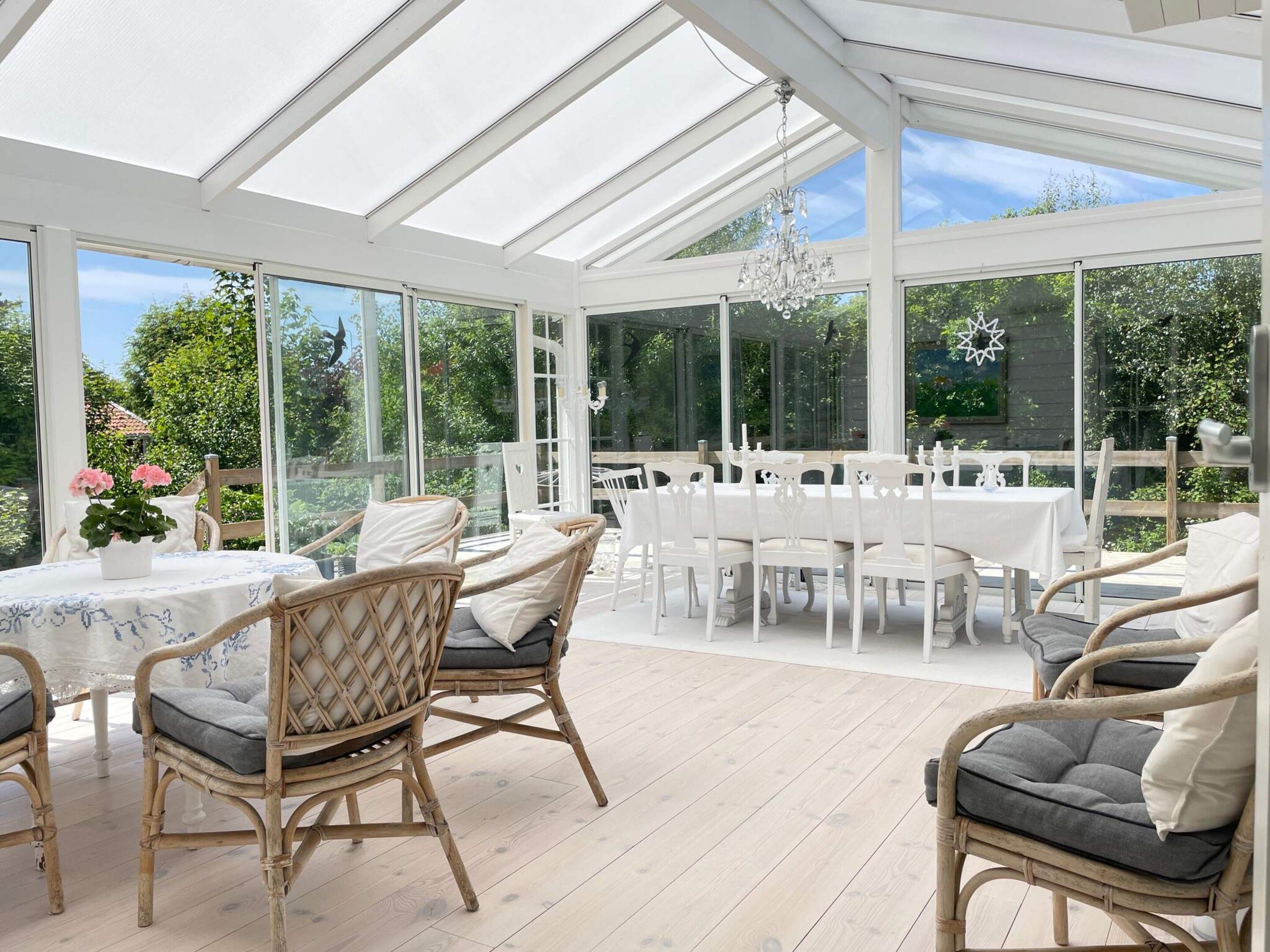 A conservatory with a glass roof, wicker furniture, and a white table set.