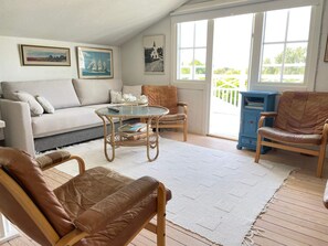 Una sala de estar acogedora con un sofá, dos sillones, una mesa de centro de vidrio y un aparador azul.