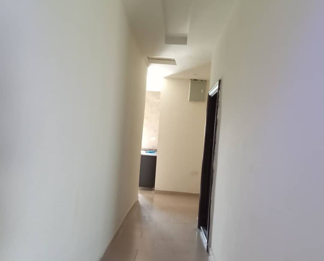 Un pasillo estrecho con suelo de tono claro que conduce a una habitación con ventana y puerta.