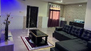 A modern living room with a black leather sofa, a glass coffee table, a flat-screen TV, and a decorative vase. - YP-MADE SUPERB VILLA featuring 2 and 1-bedroom apartments, (Ibeju Lekki)