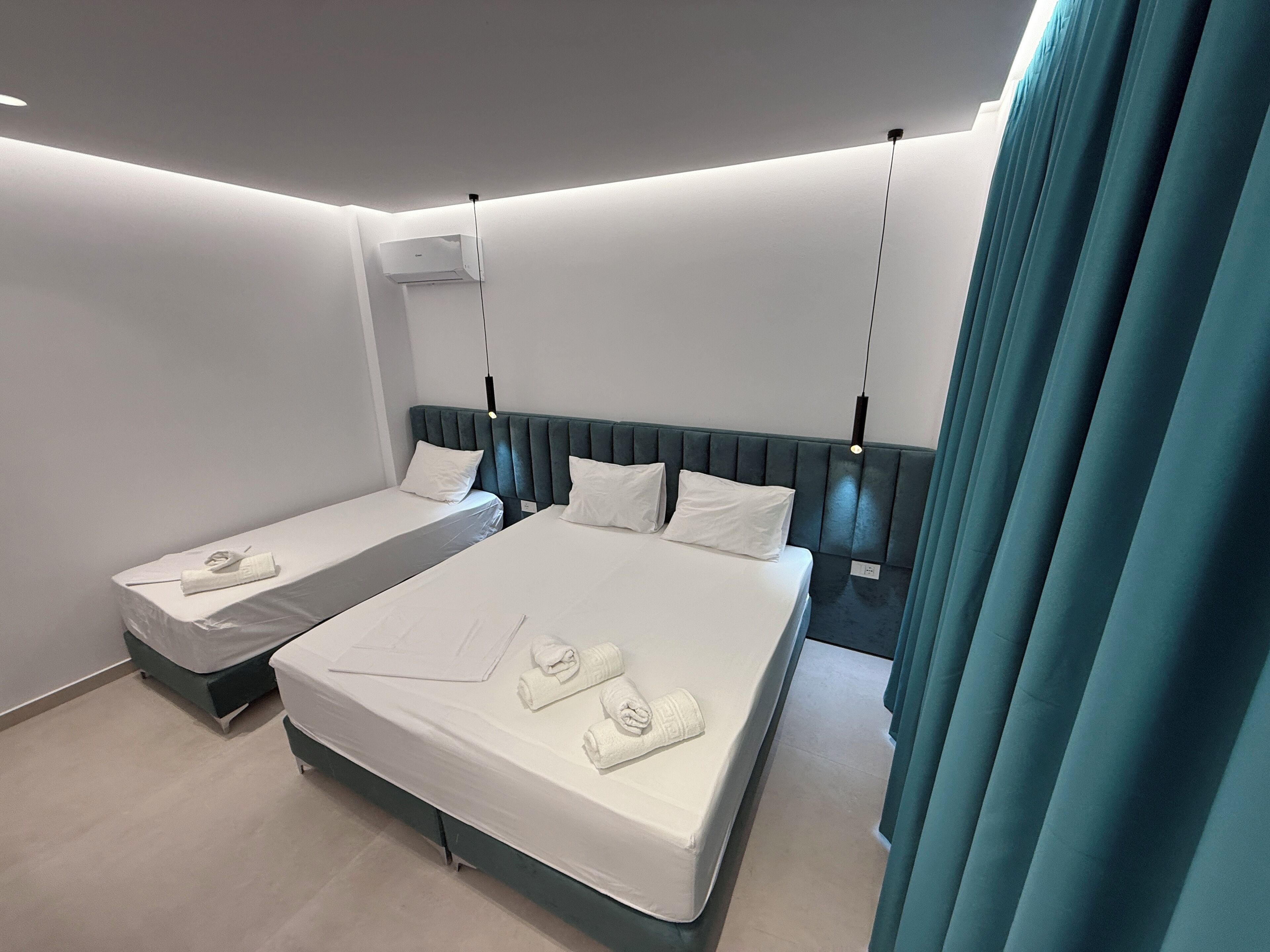 A hotel room with two beds, a large window with curtains, and a ceiling-mounted air conditioner.
