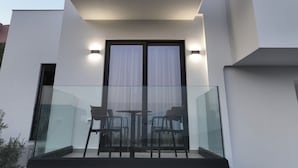 Un edificio moderno con balcón de vidrio, dos sillas y una mesa.