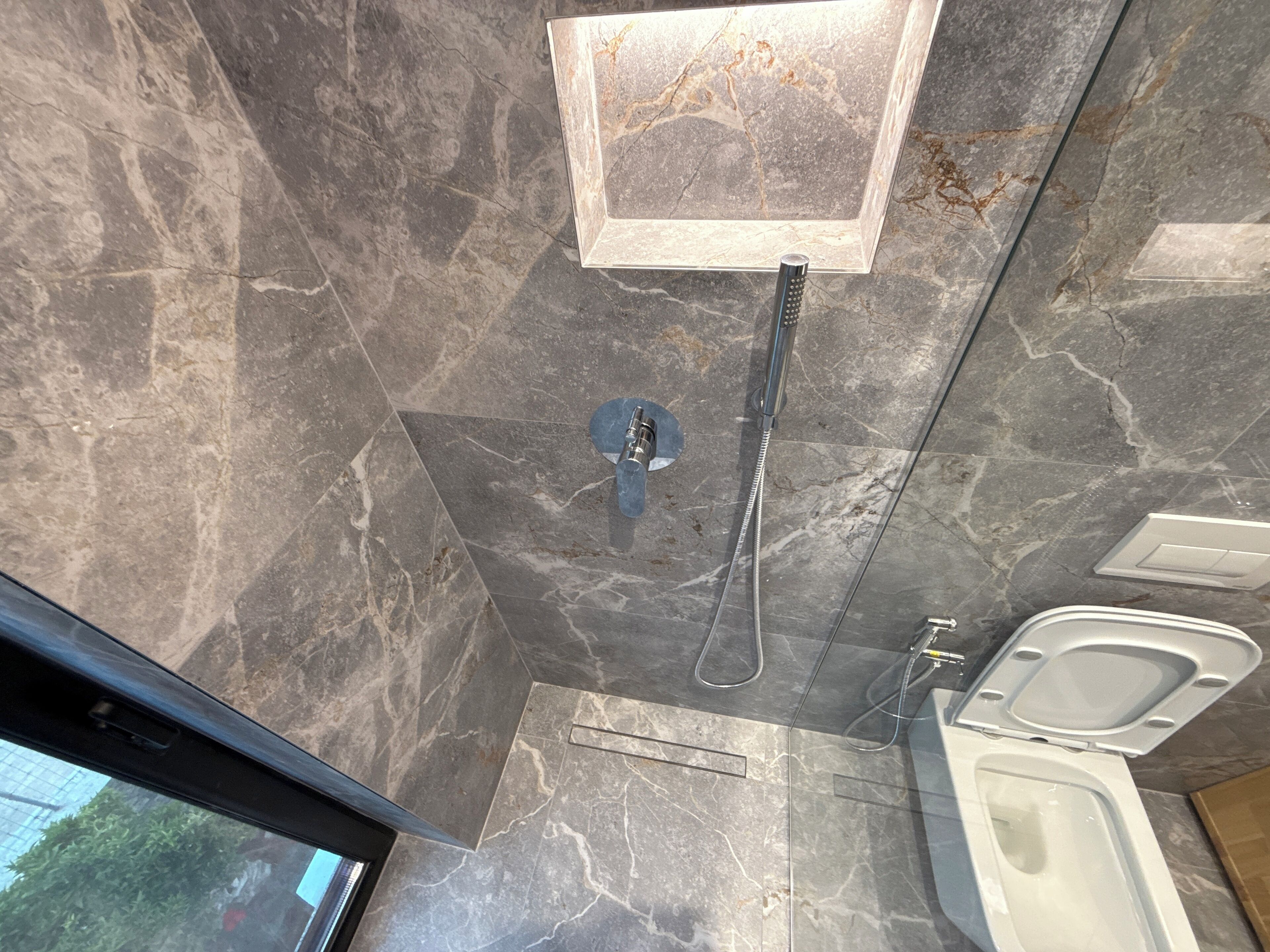 Une salle de bain avec douche, toilettes et sol en marbre.