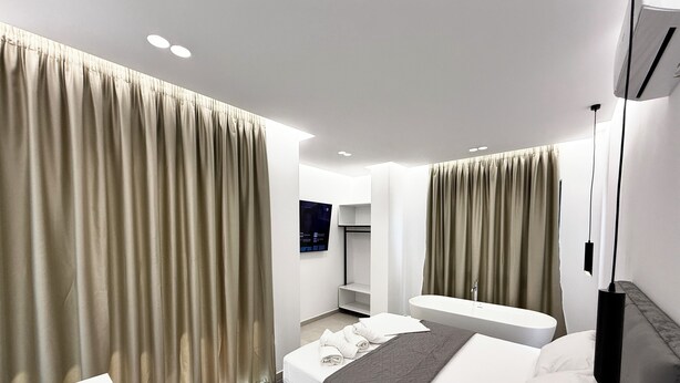 Una habitación de hotel moderna con cama, mesita de noche, banco empotrado, espejo grande y televisor de pared.