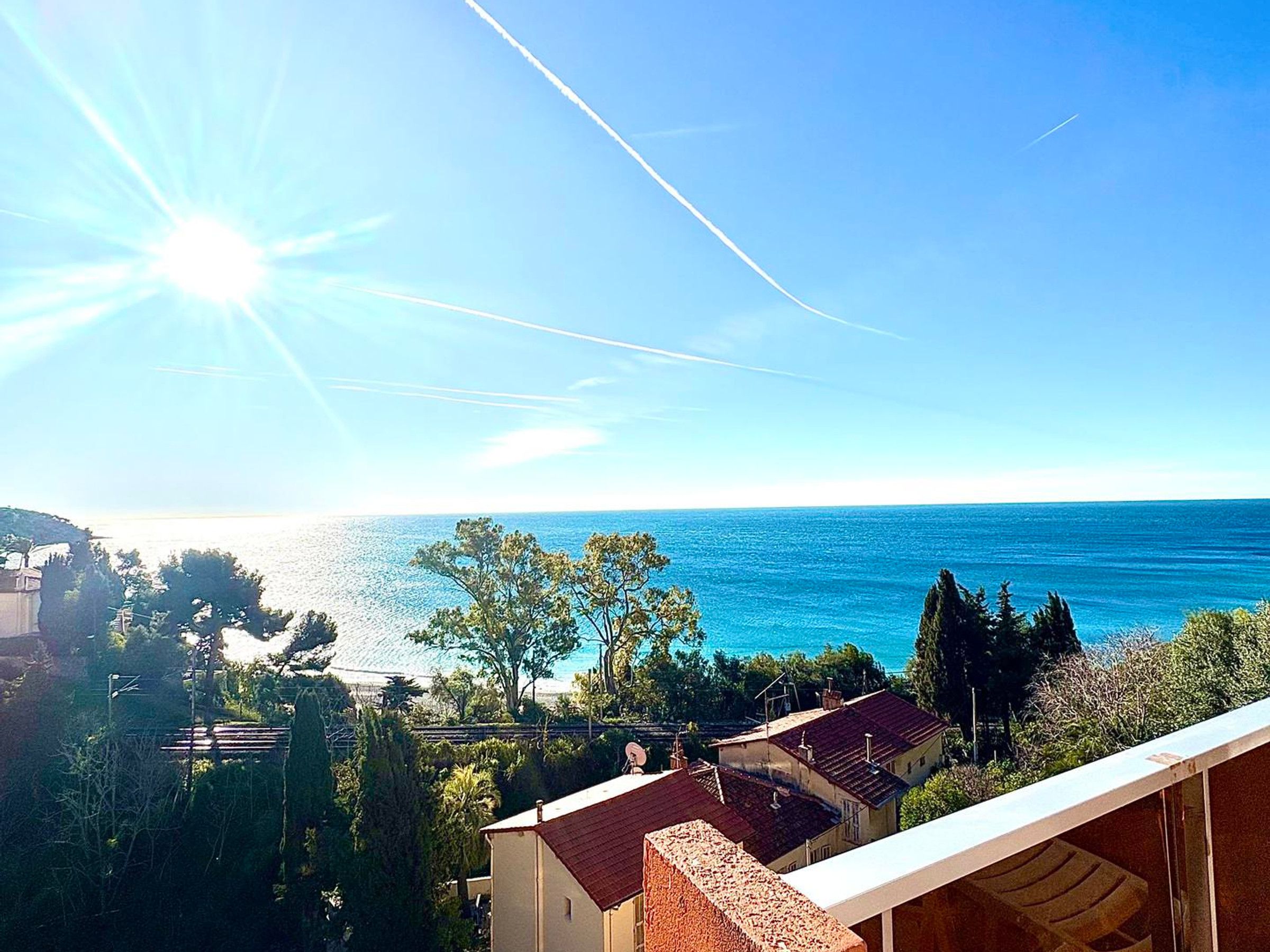A coastal view with a clear sky, a bright sun, and a calm sea.