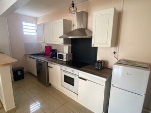 A compact kitchen with white cabinets, a stainless steel range hood, a microwave, a toaster, a dishwasher, and a refrigerator.