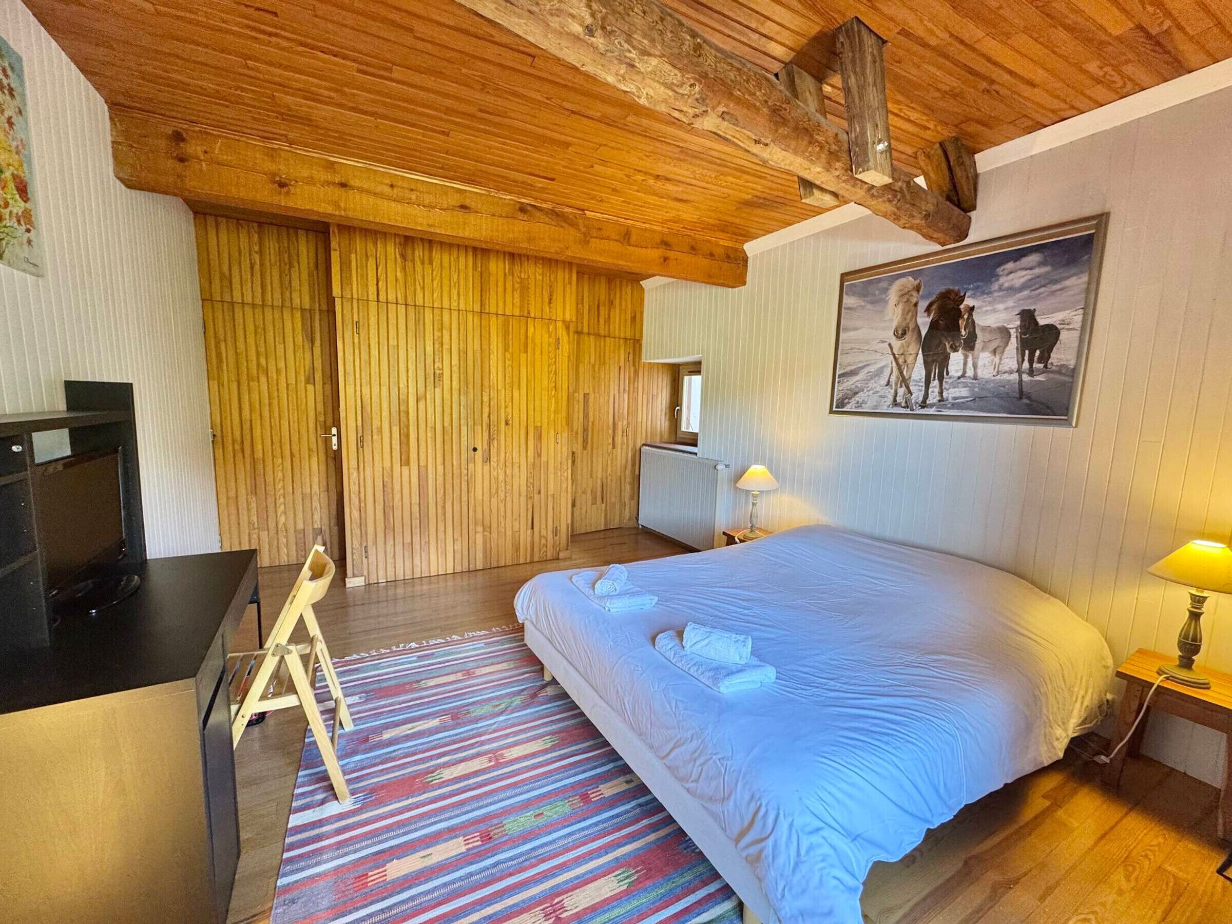 A bedroom with a bed, a desk, a chair, a lamp, and a painting on the wall.