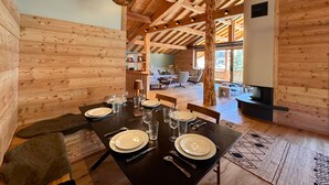 A wooden interior with a dining table set for six, a fireplace, and a view of the outdoors.
