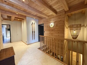 Interior de madera con una escalera, un perchero para esquíes en la pared y una lámpara colgante.