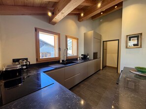 Una cocina moderna con encimera de mármol, vigas de madera y vistas a una casa a través de las ventanas.