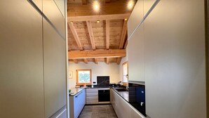 A narrow kitchen with wooden beams on the ceiling, a window with a view, and modern appliances.
