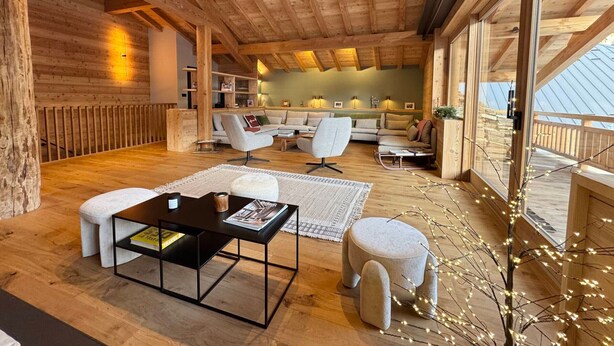 A spacious living area with wooden beams, a sofa set, a coffee table, and a dining table.