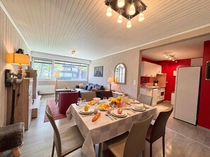 Un coin repas avec une table dressée pour quatre personnes, un canapé et une cuisine aux murs rouges.
