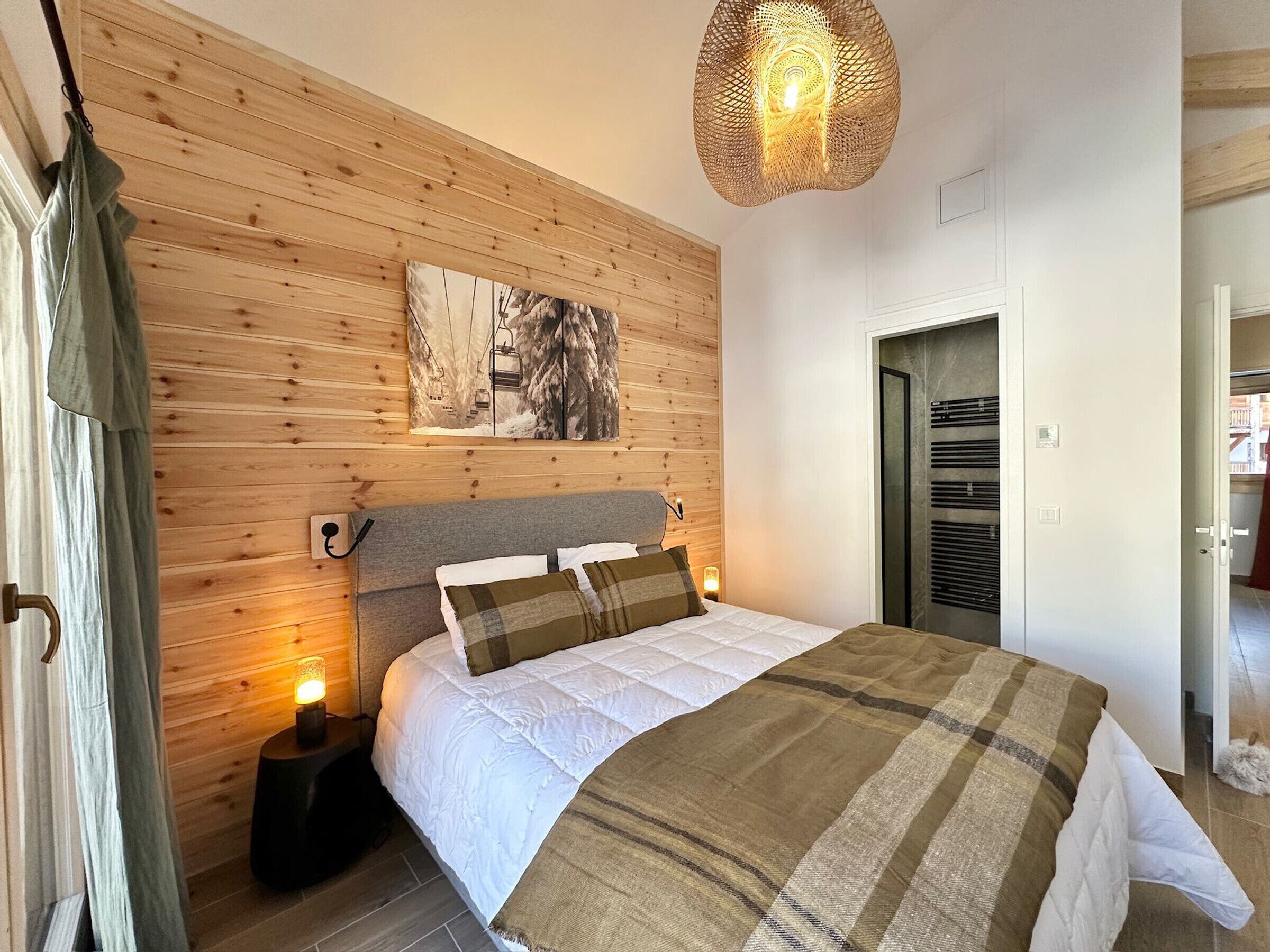 A bedroom with a wooden wall, a bed with white and brown bedding, a hanging light fixture, and a door with a window.