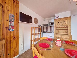 Ein Essbereich mit einem Holztisch, gedeckt für vier Personen, einem an der Wand montierten Fernseher und einer Küche mit weißen Schränken und einer Mikrowelle.