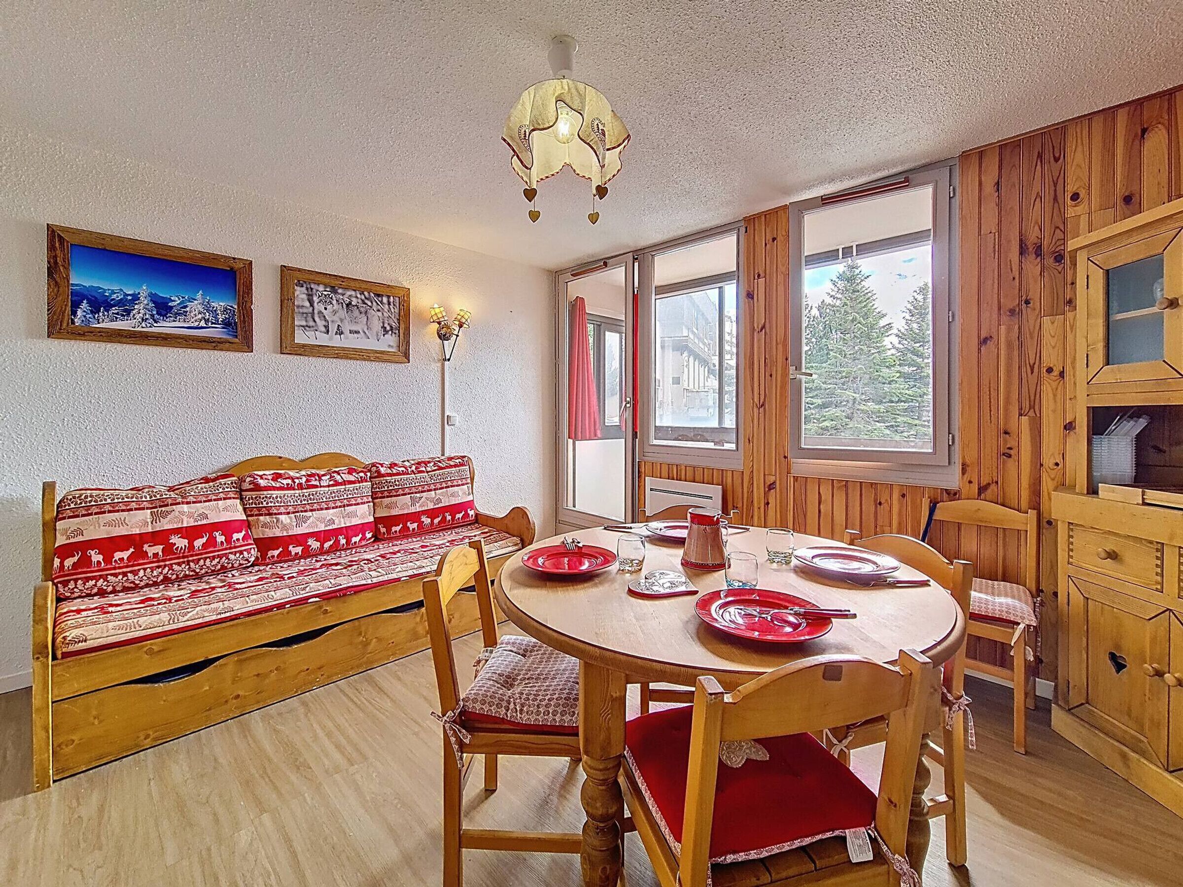 A cozy room with a wooden bench, a dining table with chairs, and a large window offering a view of trees.