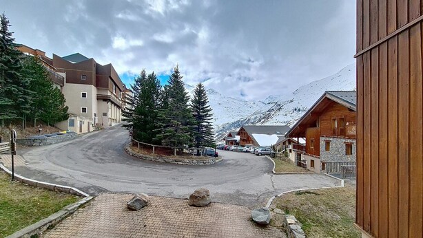 Ein gepflasterter Weg führt zu einem Gebäude mit Holzfassade, umgeben von schneebedeckten Bergen und einigen Bäumen.