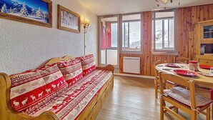 Ein gemütliches Zimmer mit einer Holzsofa, einem Esstisch mit Stühlen und großen Fenstern mit Blick auf schneebedeckte Berge.
