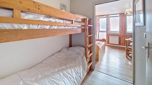 Ein Schlafraum mit Etagenbetten, einem Holzkopfende, einer Holztür und Blick auf einen Essbereich durch eine Glastür.