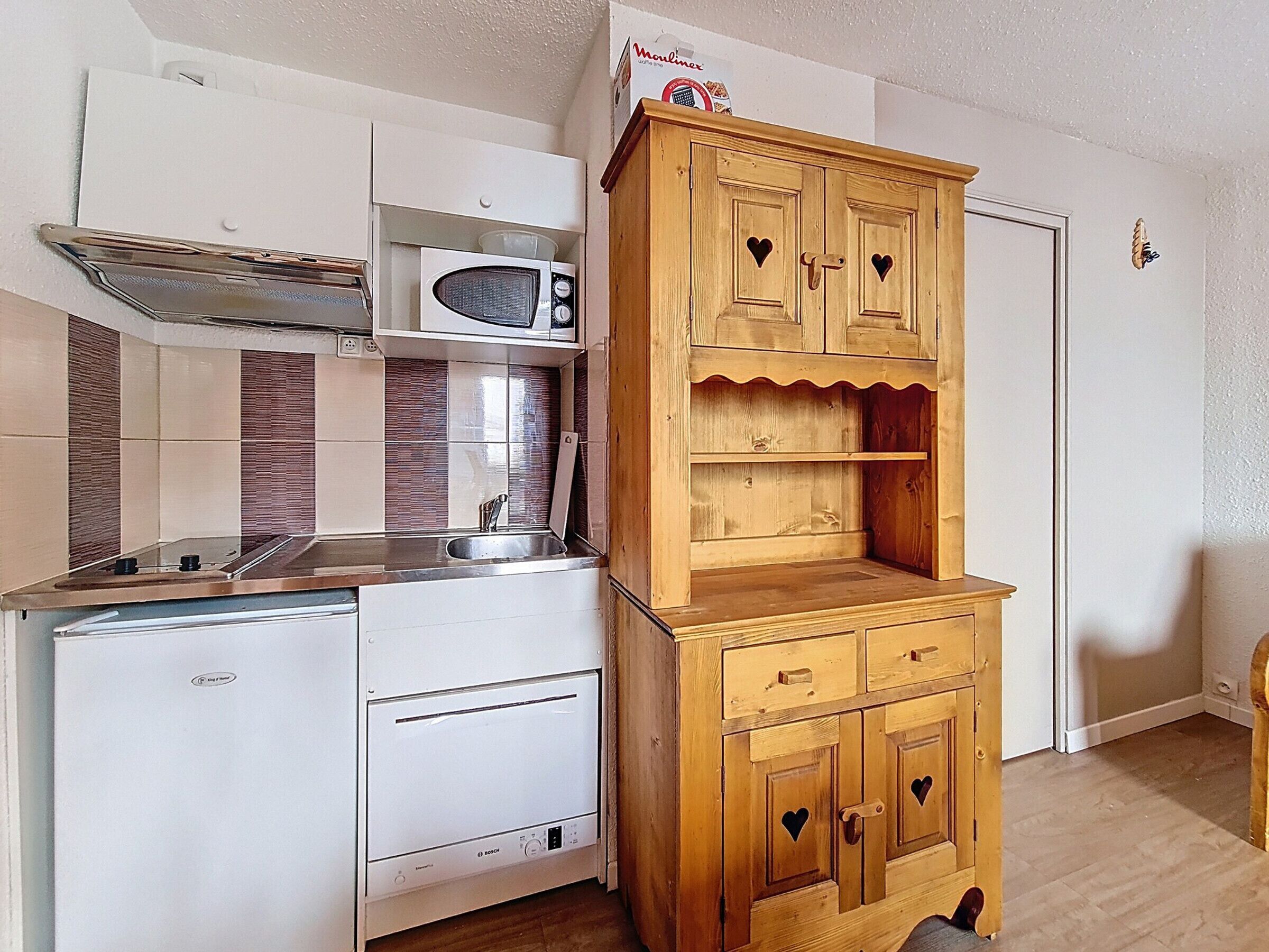 Une cuisine compacte équipée d’un four à micro-ondes, d’une cuisinière et d’un meuble en bois orné de découpes en forme de cœur.