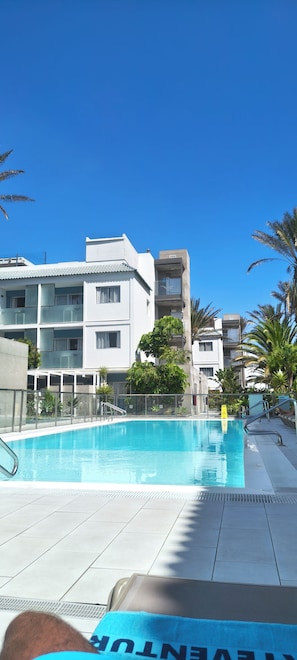 A swimming pool with a tiled deck, surrounded by buildings with balconies and some greenery.
