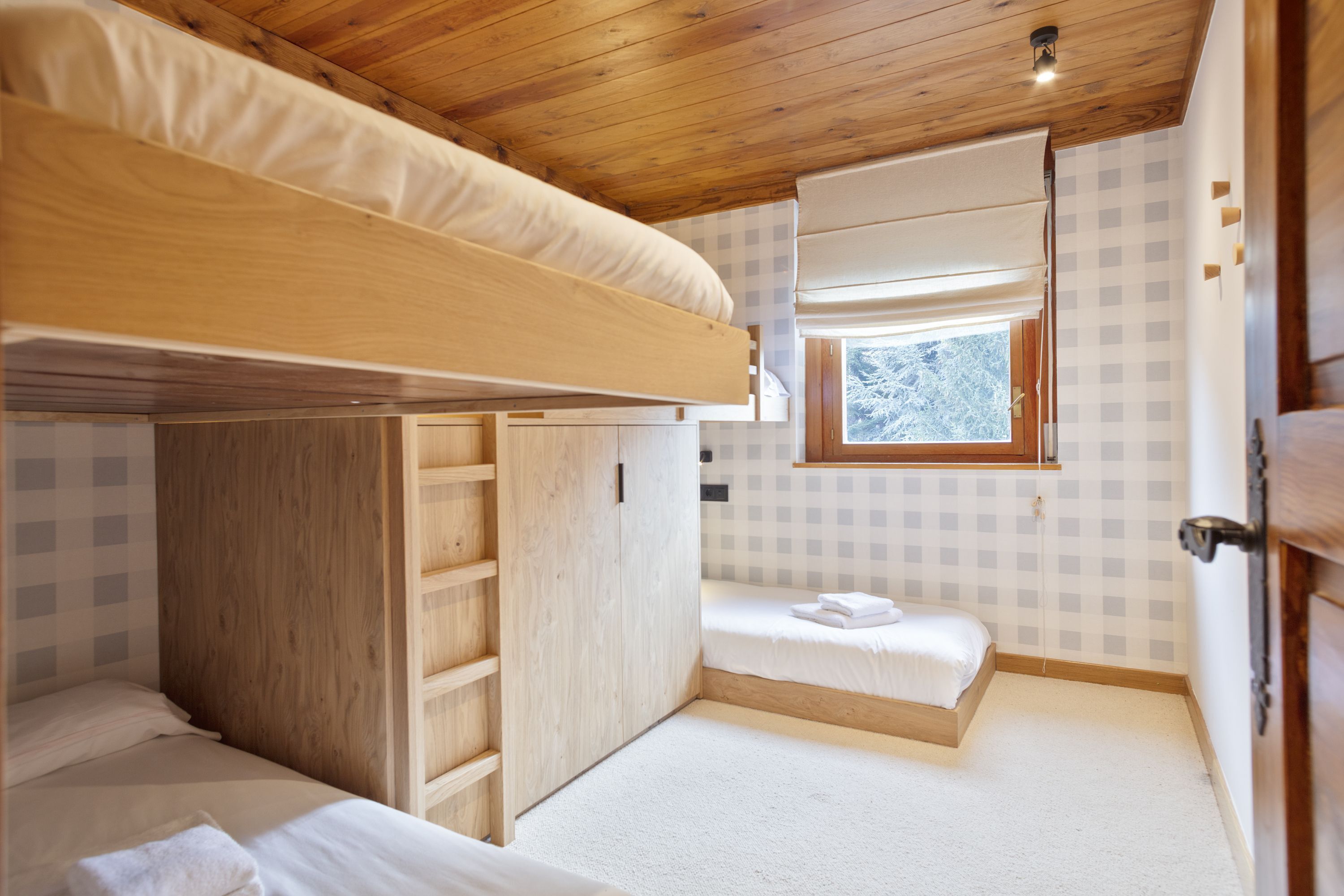 Habitación pequeña con literas, un escritorio y ventana con vistas a árboles.