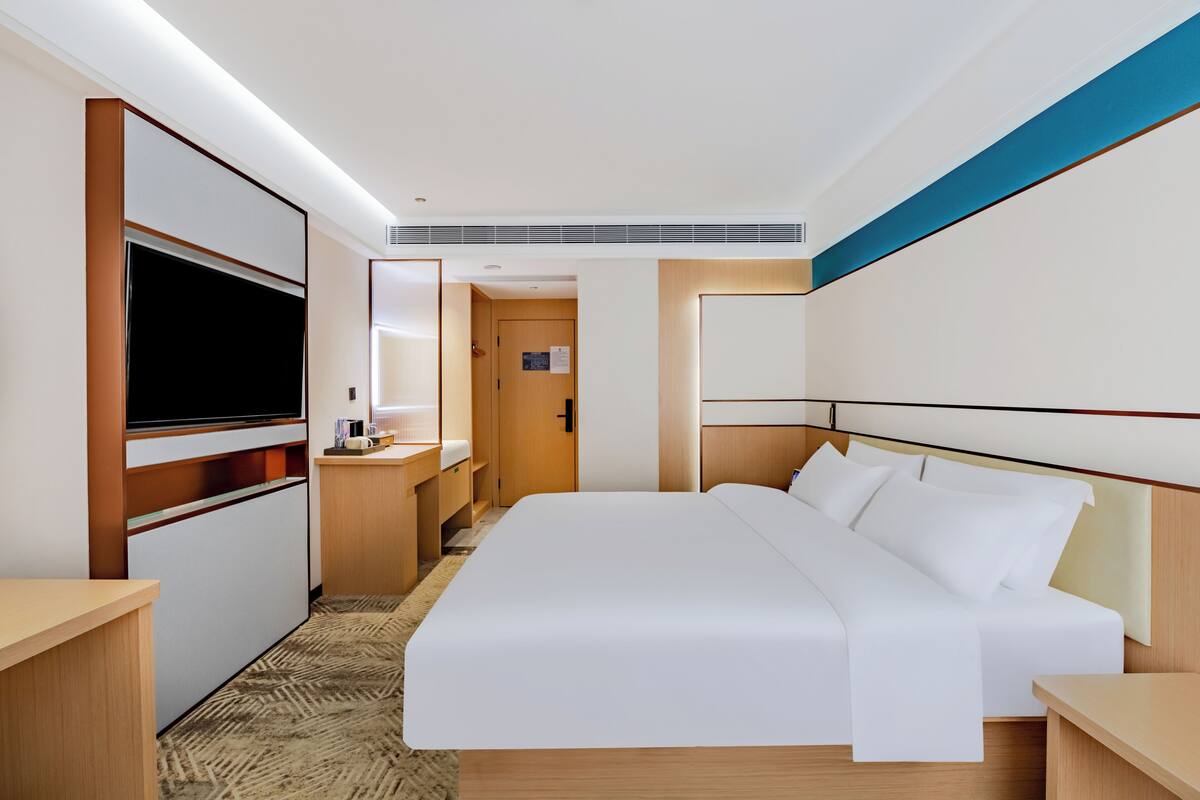 A hotel room with a large bed, a TV, a desk, and a bathroom.