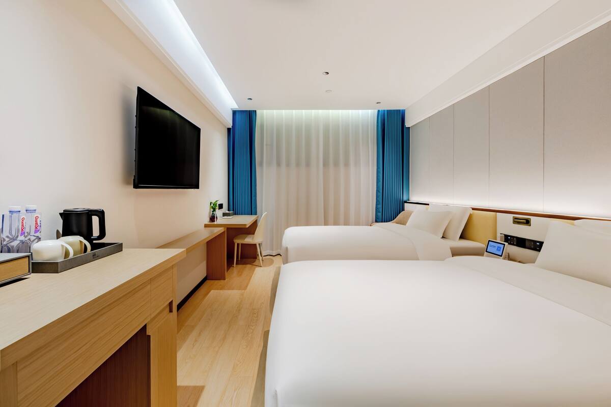 A hotel room with two beds, a desk, a flat-screen TV, a coffee maker, and a small table with a laptop.