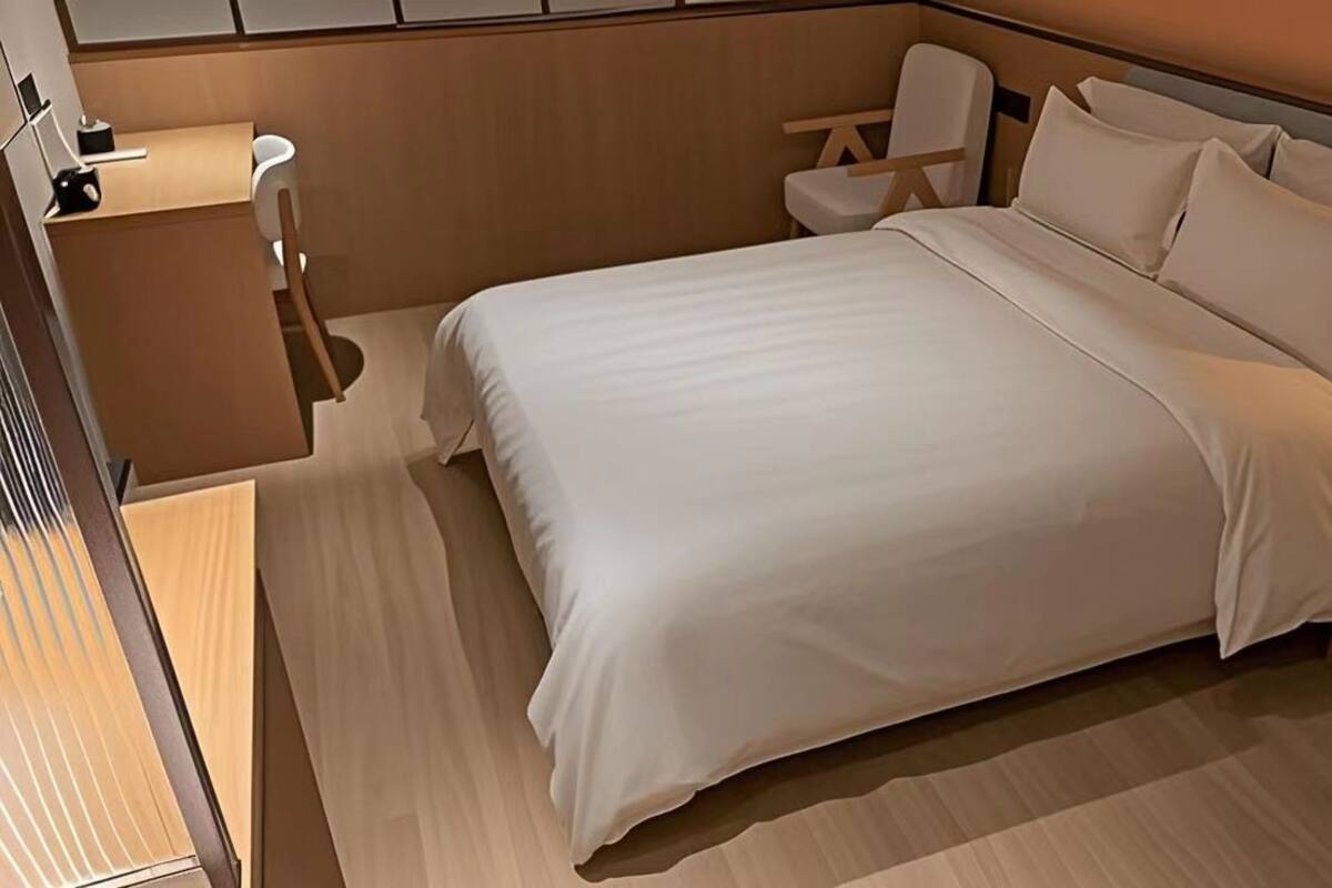 A hotel room with a large bed, a desk, a chair, and a bedside table.