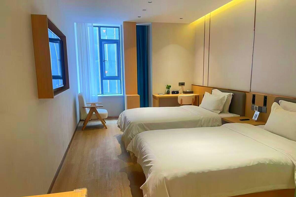 A hotel room with two beds, a desk, a chair, and a window with curtains.