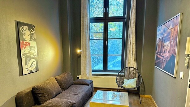 A modern living room with a dark brown sofa, a glass coffee table, and a large window with curtains. - Beautiful apartment in the trendy Ottensen district near the S-Bahn (Hamburg)