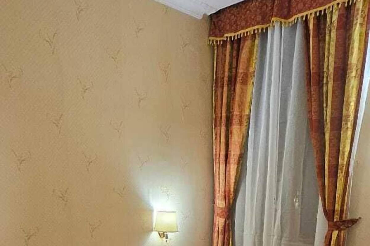 A hotel room with a double bed, two pillows, a bedside lamp, and a window with curtains.