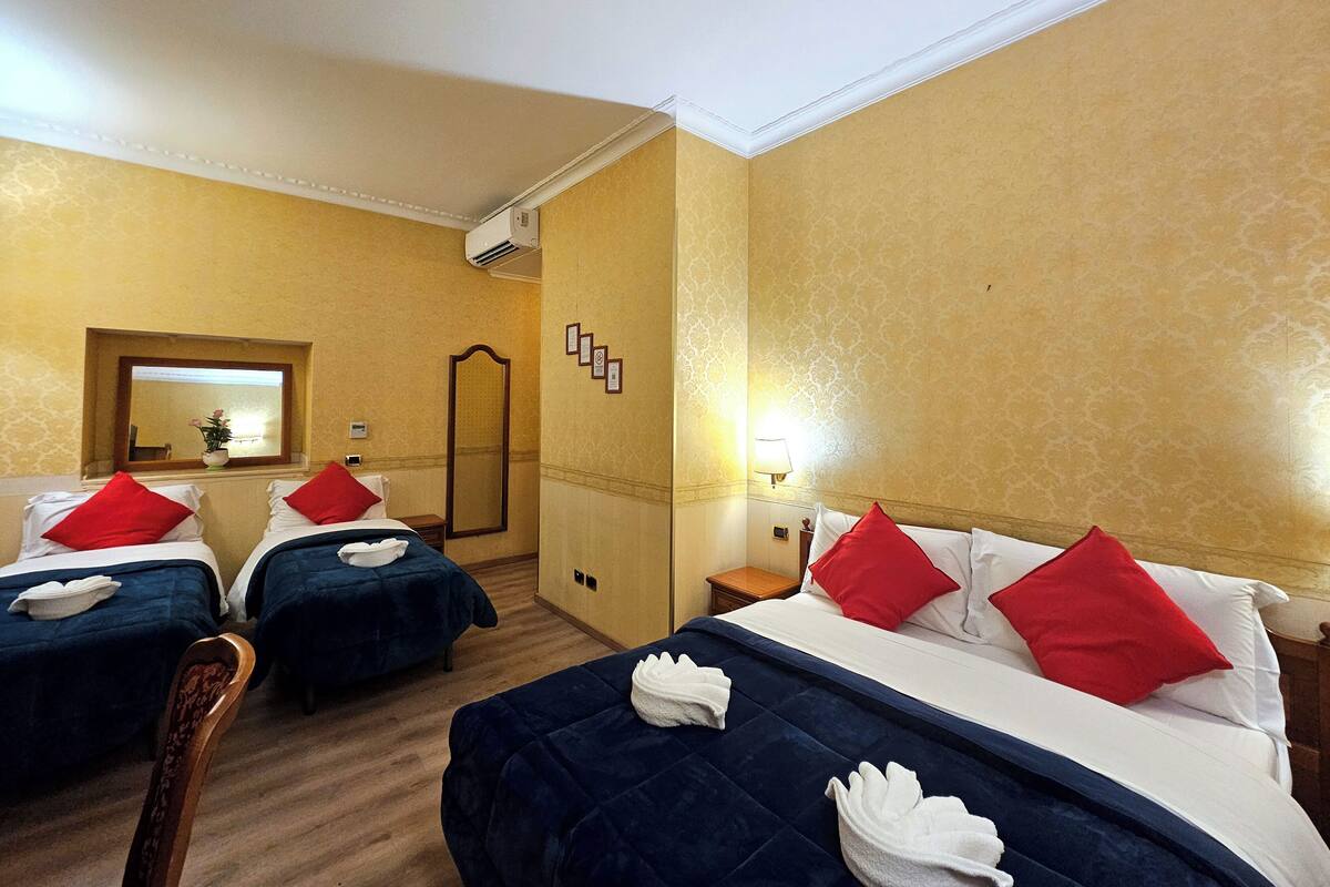 A hotel room with two beds, each with red and white pillows, and a large mirror on the wall.