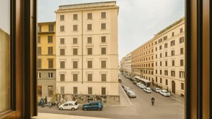 A multi-story building with a uniform facade, parked cars along the street, and a pedestrian walkway. - Hotel Amadeus (Rome)