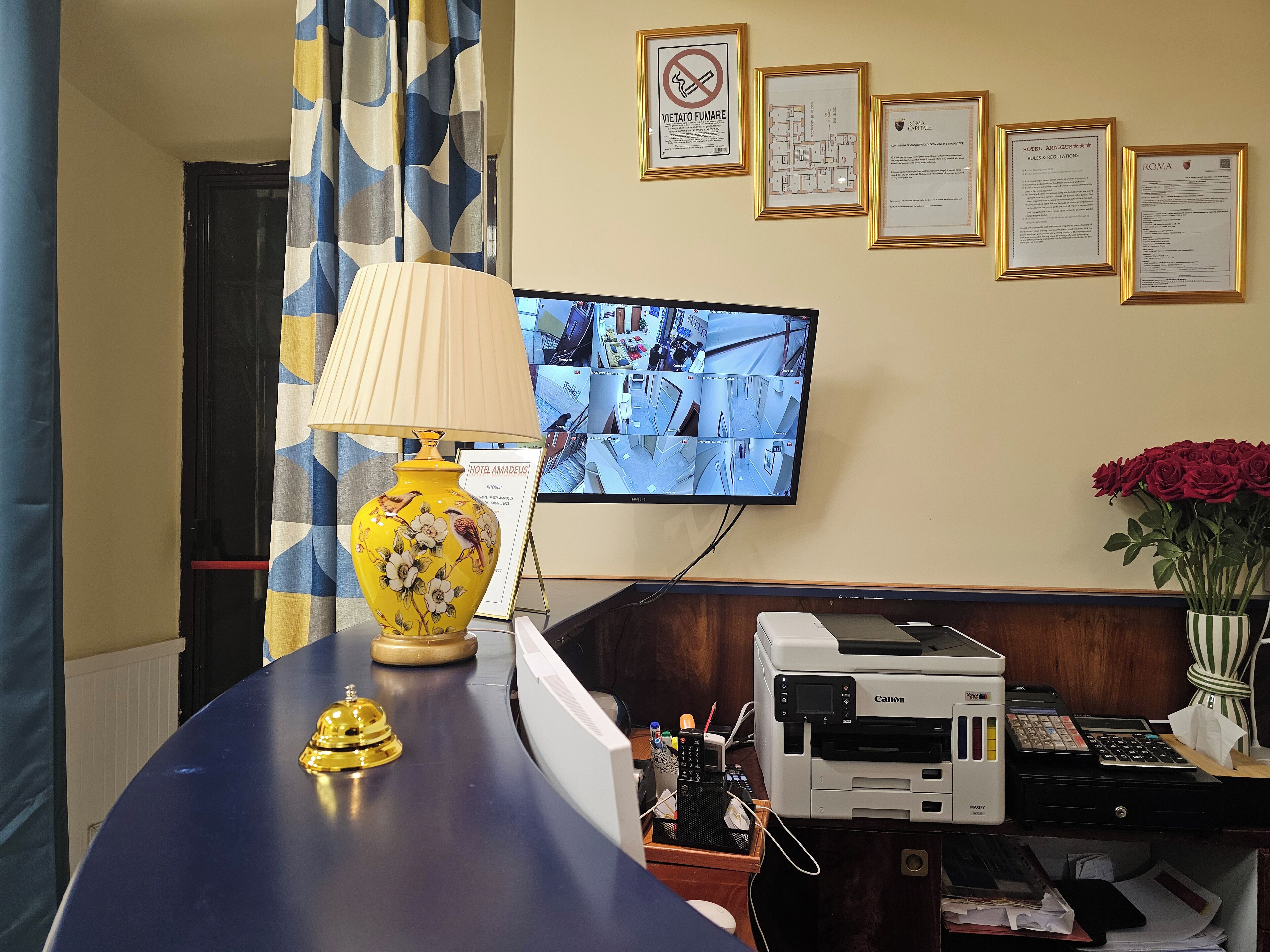 A reception desk with a yellow vase, a lamp, and a monitor displaying security cameras.