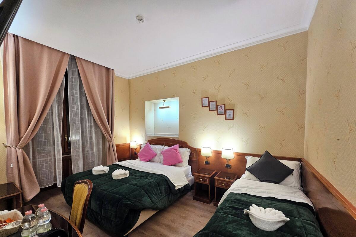 A hotel room with two beds, a desk with a chair, a mirror, and a wall with framed certificates.